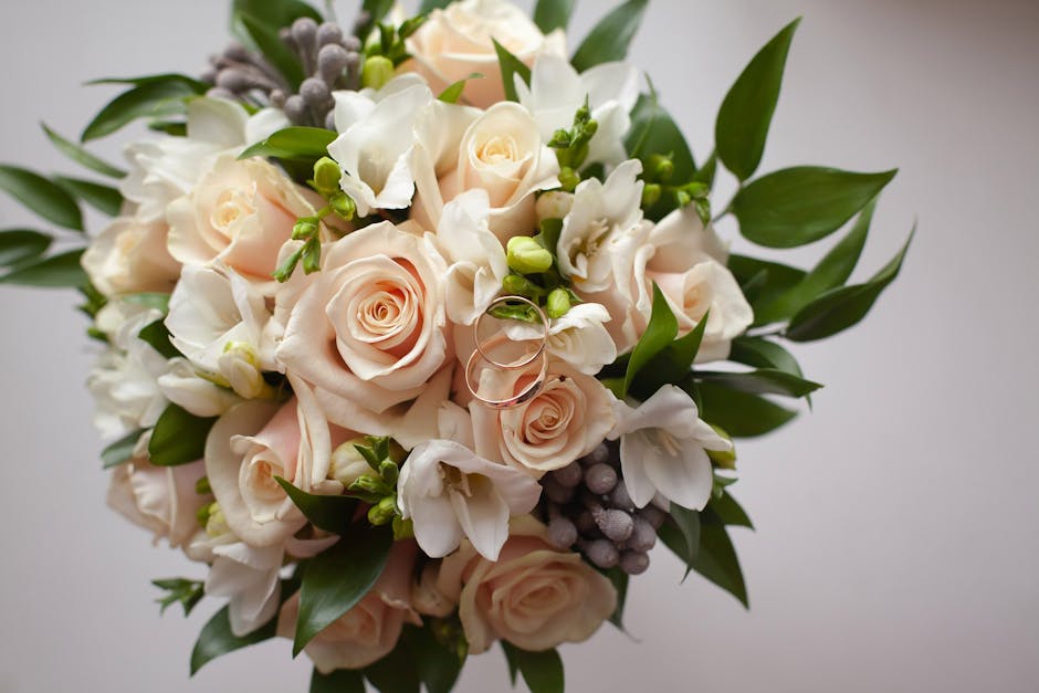 A close-up of a floral arrangement featuring soft pink roses with delicate, tightly curled petals, complemented by white freesias with slender, arching stems and small bell-shaped blossoms. The bouque